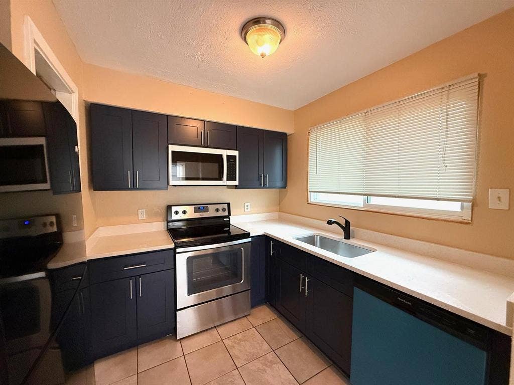 2705 Tanglewood Drive, Lancaster, TX 75134 Galley kitchen featuring dark blue cabinetry, stainless steel appliances, light-toned countertops, and tile flooring