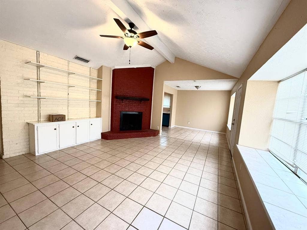 2705 Tanglewood Drive, Lancaster, TX 75134 Vaulted ceiling with a ceiling fan, tiled flooring, brick accent wall with built-in shelving and cabinetry, and a brick fireplace