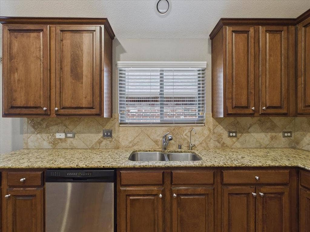 Kitchen featuring wood cabinetry, granite-style countertops, a stainless steel double-basin sink, and a tiled backsplash