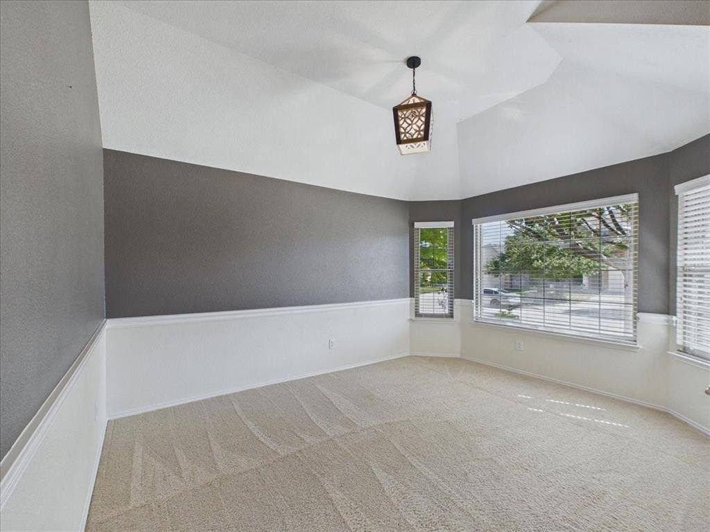 Vaulted ceiling with an ornamental pendant light, large bay window, and a secondary window, featuring two-tone walls with wainscoting and carpeting