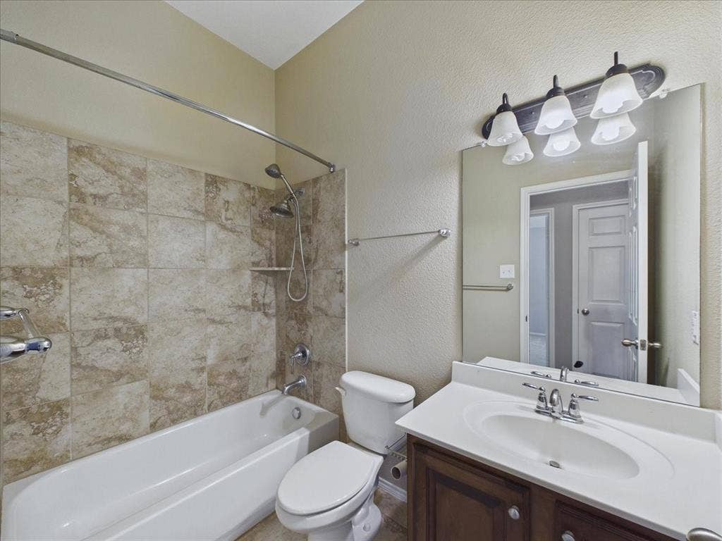 Bathroom featuring a built-in tub with tile surround, a dark wood-finish vanity with an integrated sink, a large wall-mounted mirror, and a multi-bulb vanity light fixture