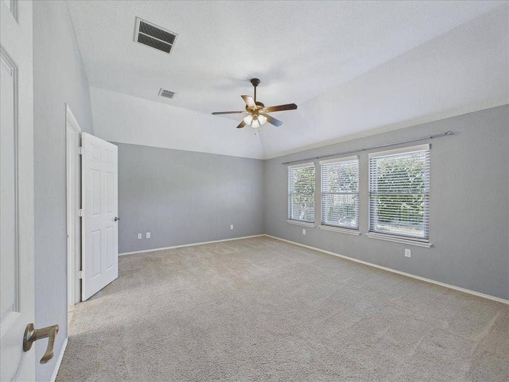 Vaulted ceiling with a ceiling fan, three windows, and neutral carpeting