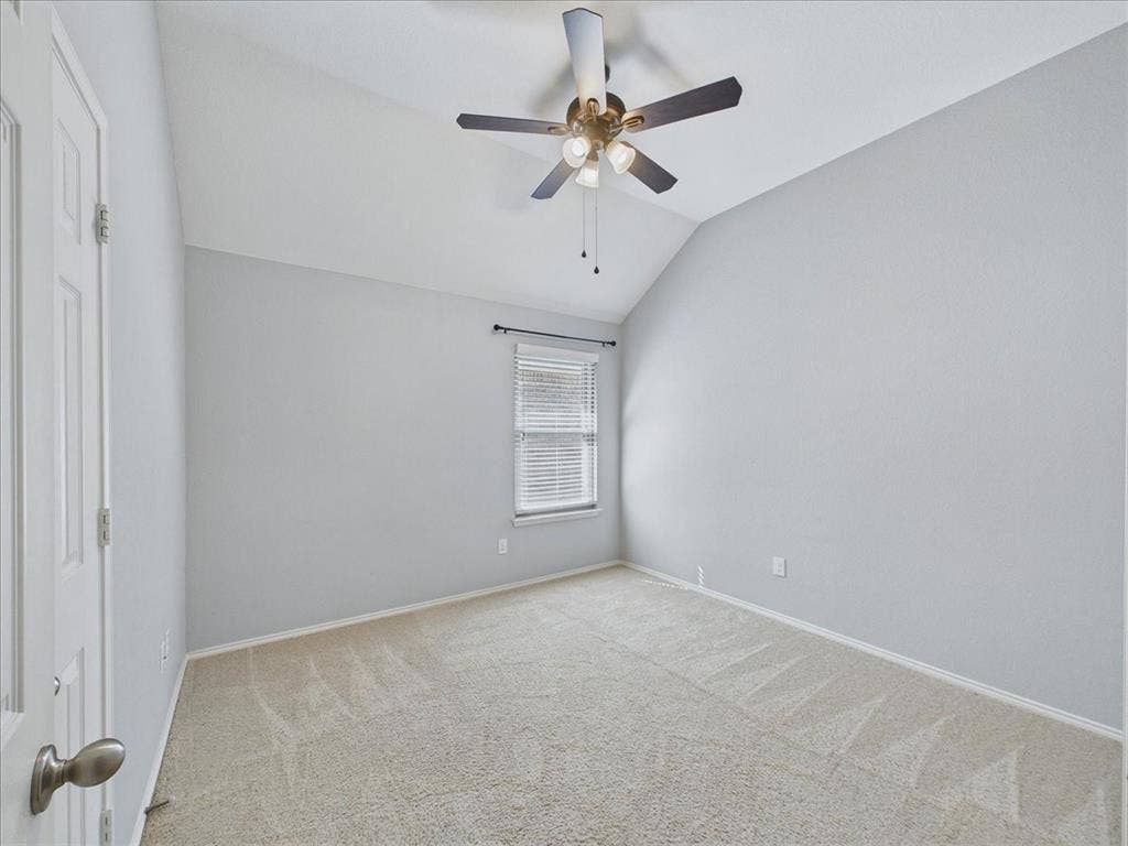 Vaulted ceiling, ceiling fan with integrated lighting, neutral wall finishes, light-colored carpeting, and window with blinds