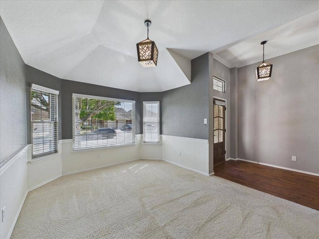 Vaulted ceiling with decorative pendant lighting, bay window, two-tone wall treatment, and wood-finish flooring at entry