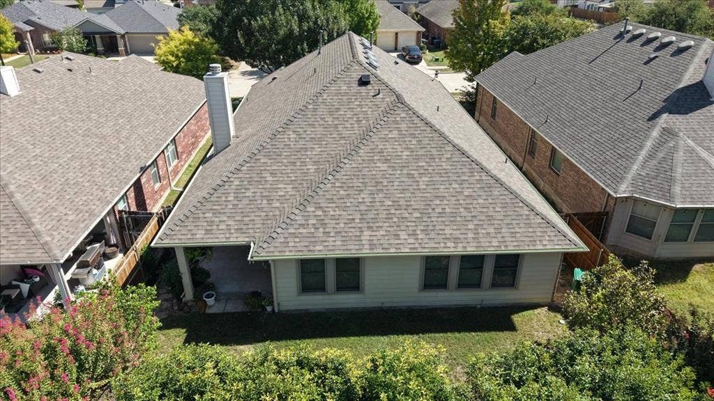 Architectural shingle roof, covered patio, multiple windows, established perimeter landscaping, and a fenced property line