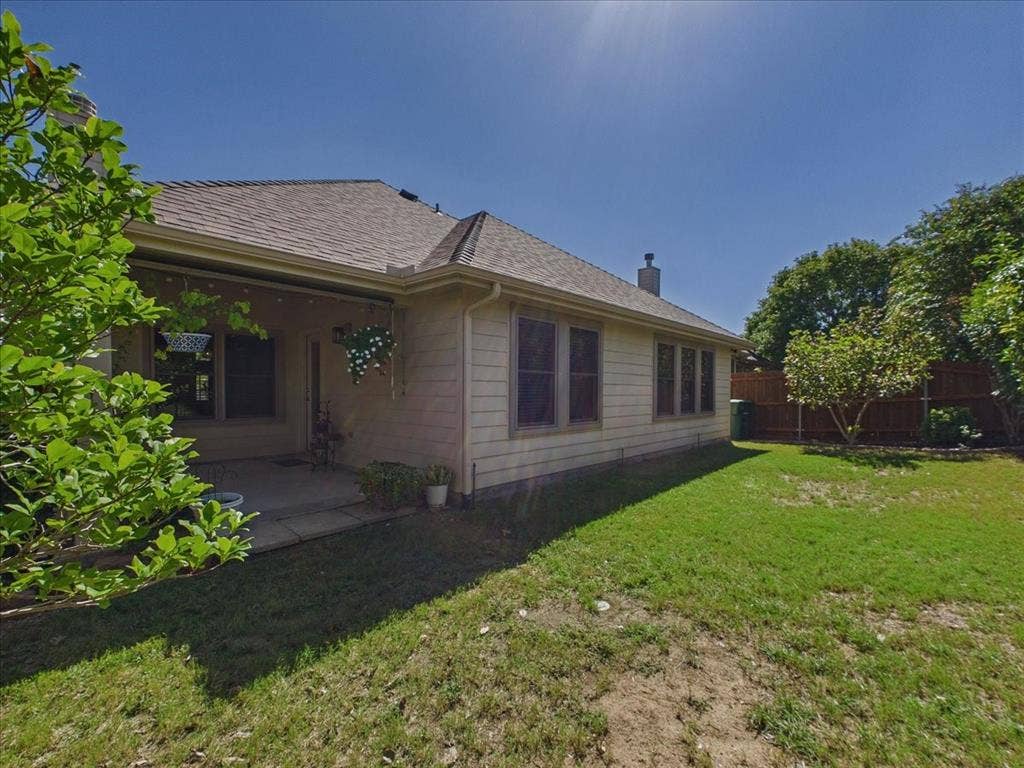 Expansive lawn area with mature trees, covered patio, and a privacy fence