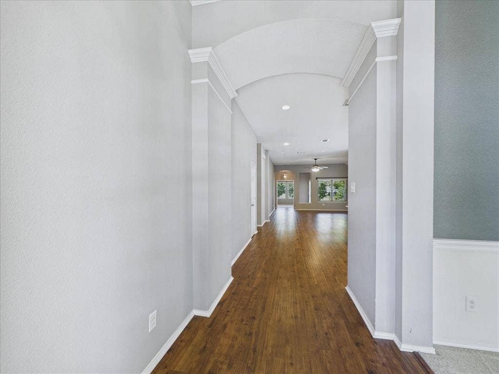 Hallway with wood-finish flooring, an arched entryway, recessed lighting, crown molding, and wainscoting