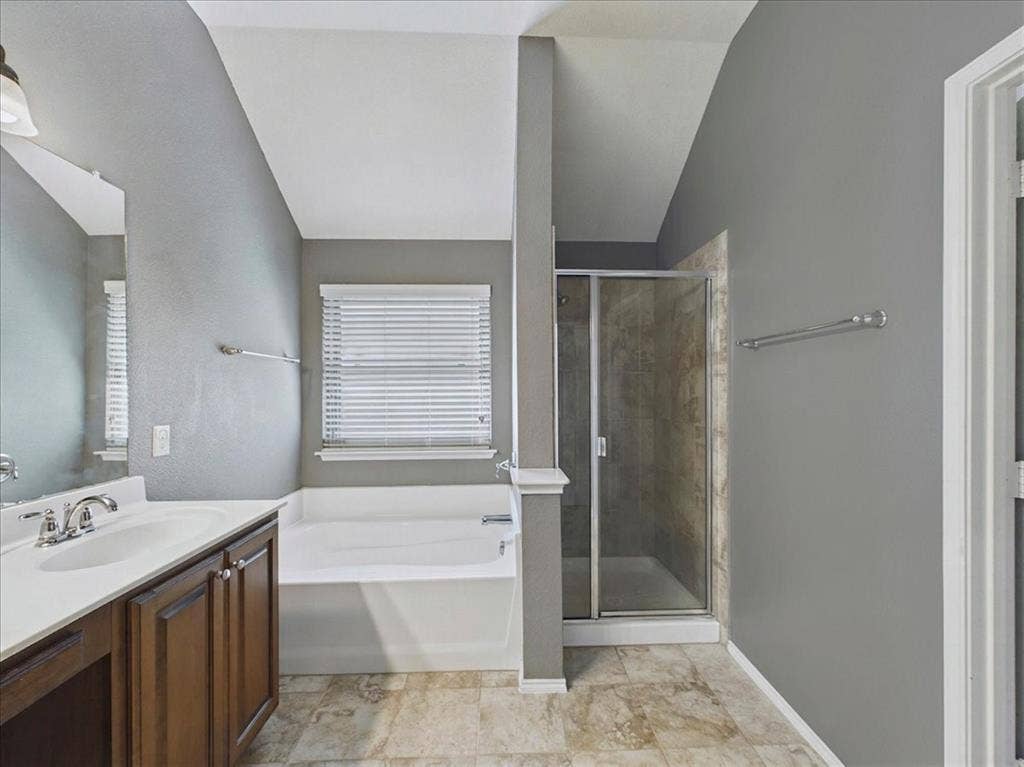 Bathroom featuring a built-in tub, separate shower enclosure with glass door, single vanity with wood-finish cabinetry and white countertop, and tiled flooring