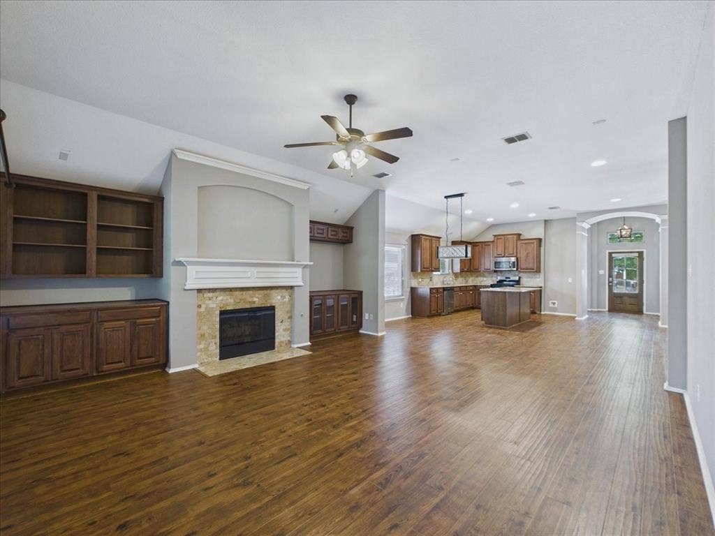 Open-concept living space featuring wood-finish flooring, a stone-surround fireplace with built-in cabinetry, and a ceiling fan