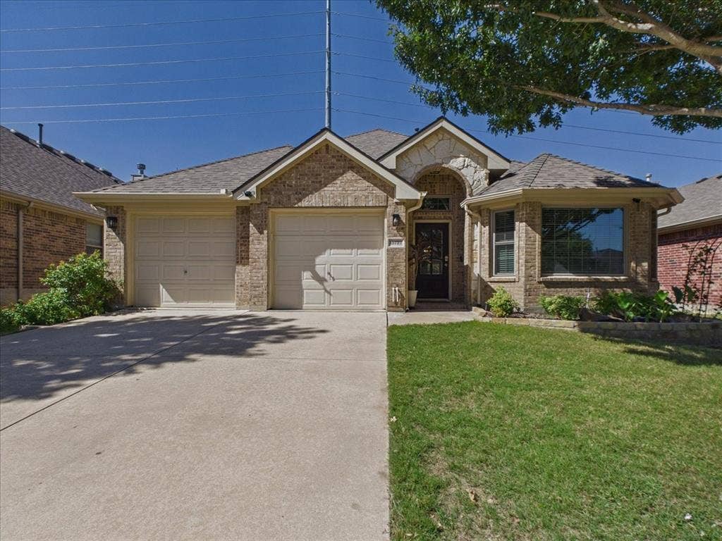 Brick exterior with stone accents, an attached two-car garage, a concrete driveway, and a front lawn with mature landscaping