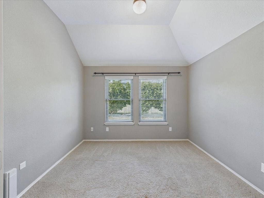 Vaulted ceiling, two windows with blinds, neutral carpet, and recessed lighting