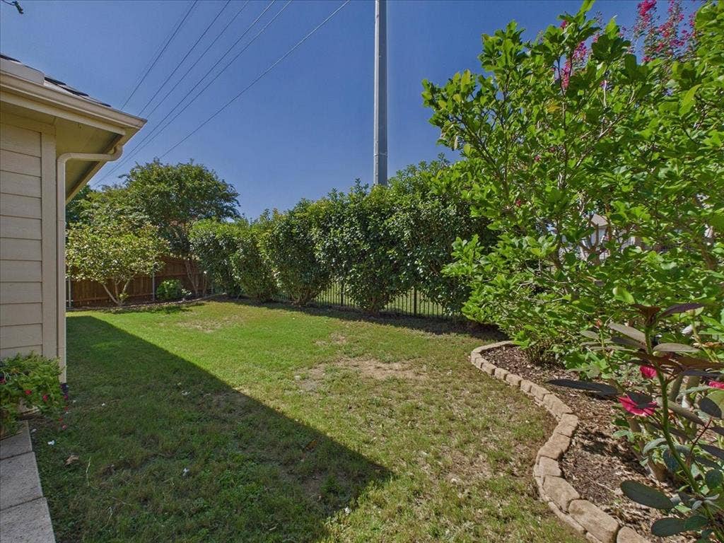 Expansive lawn area with mature shrubs and trees, framed by a decorative stone border and black metal fencing