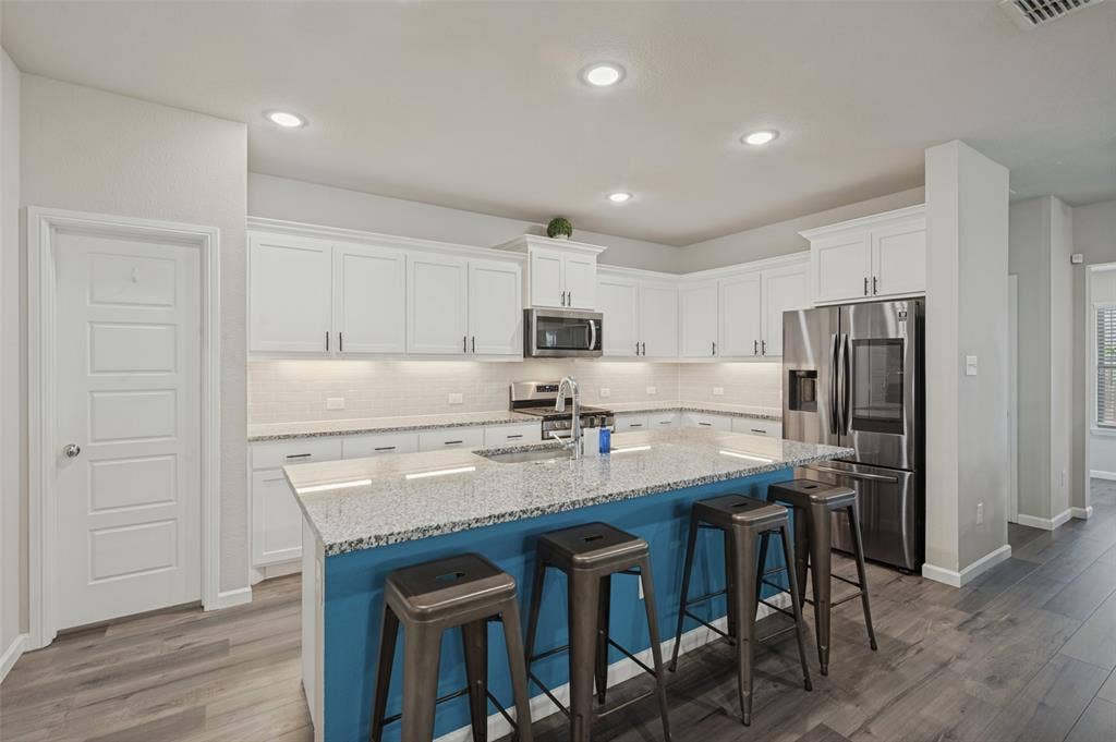 632 Cherry Hills Road, Red Oak, TX 75154 Kitchen featuring an expansive island with a blue base and light-colored countertop, white upper and lower cabinetry, stainless steel appliances, and wood-finish flooring