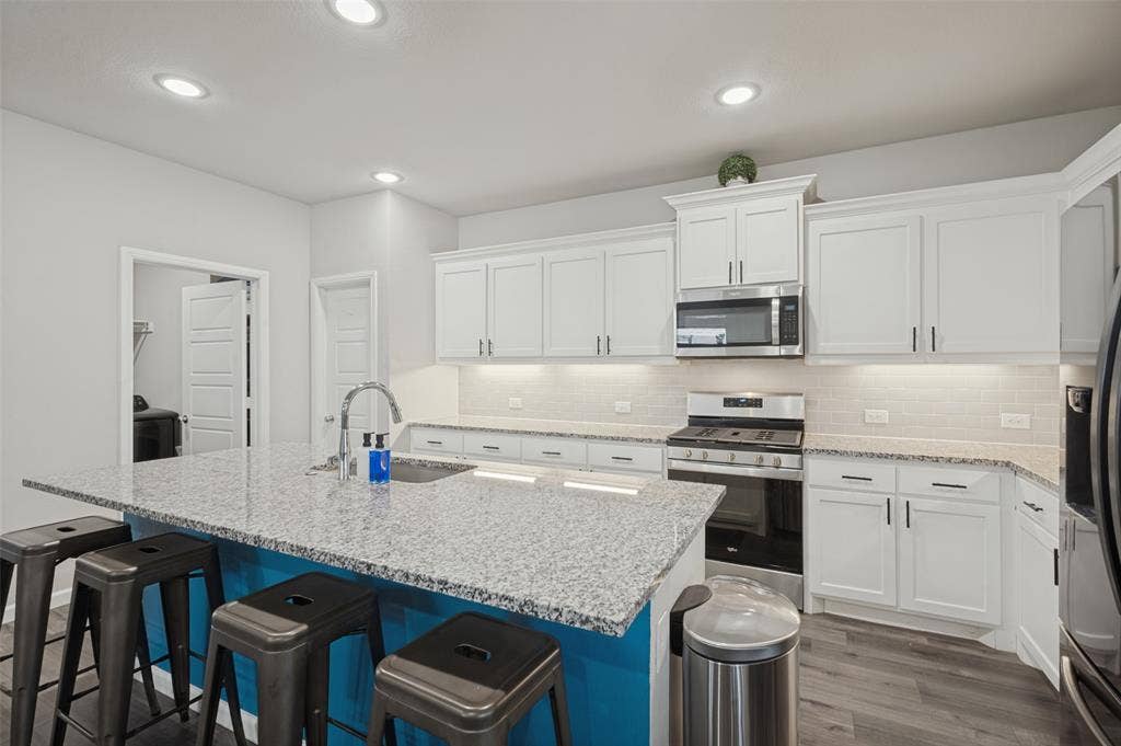 632 Cherry Hills Road, Red Oak, TX 75154 Kitchen featuring a central island with a sink and seating, white cabinetry, stainless steel appliances, granite countertops, and wood-finish flooring