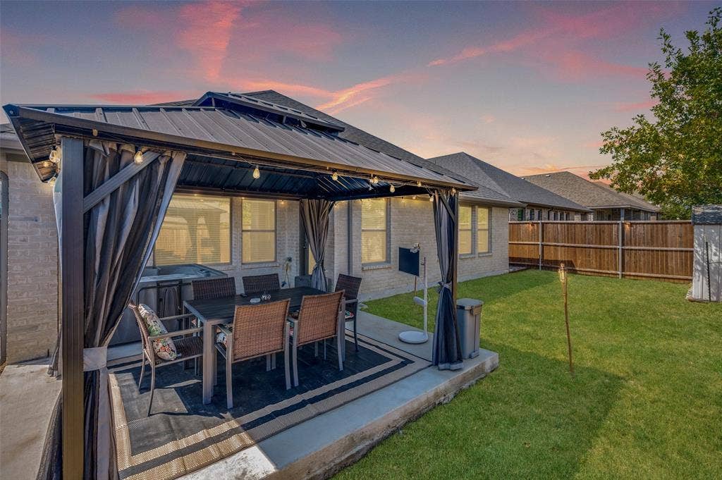 632 Cherry Hills Road, Red Oak, TX 75154 Covered patio with string lighting, surrounded by a fenced backyard featuring a grassy area and brick exterior
