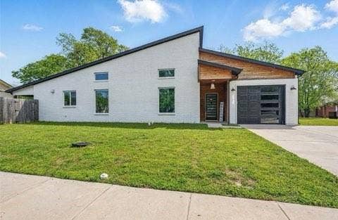 Modern exterior featuring a painted brick facade, asymmetrical roofline, wood-panel accenting, and a garage door with horizontal glass panels