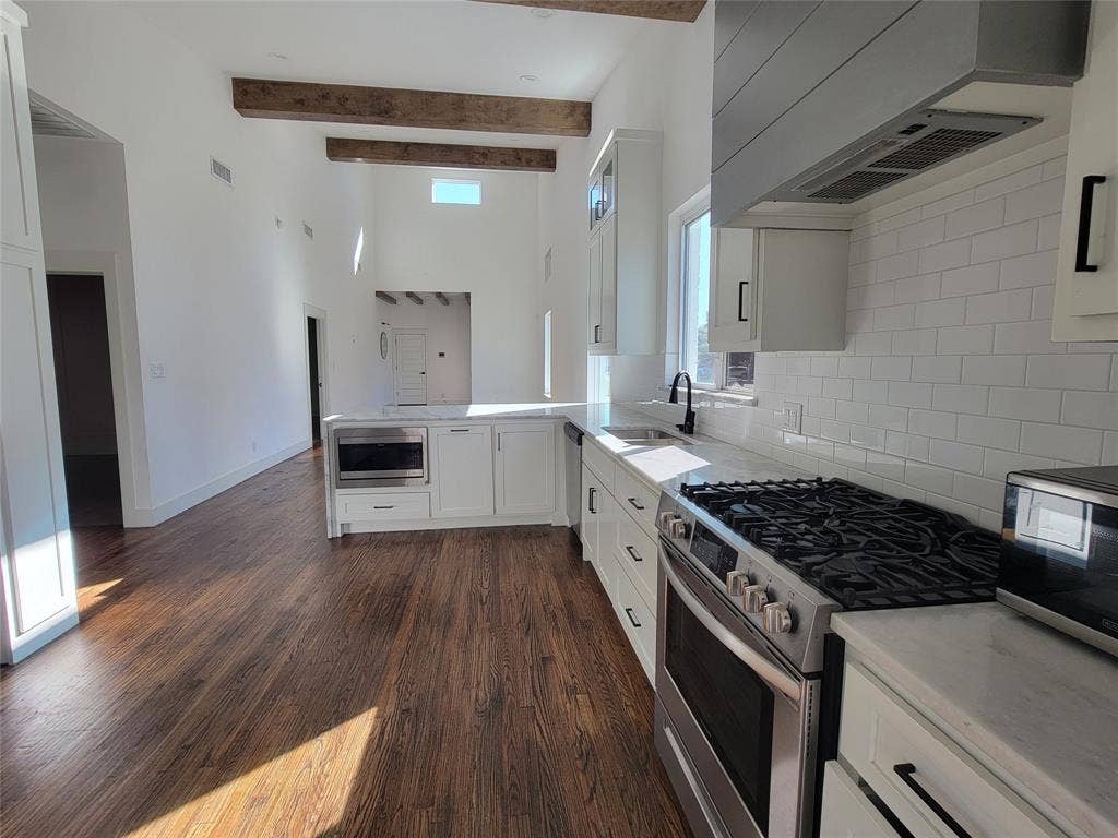 Kitchen featuring wood-finish flooring, vaulted ceilings with exposed wood beams, white cabinetry, subway tile backsplash, and a gas range