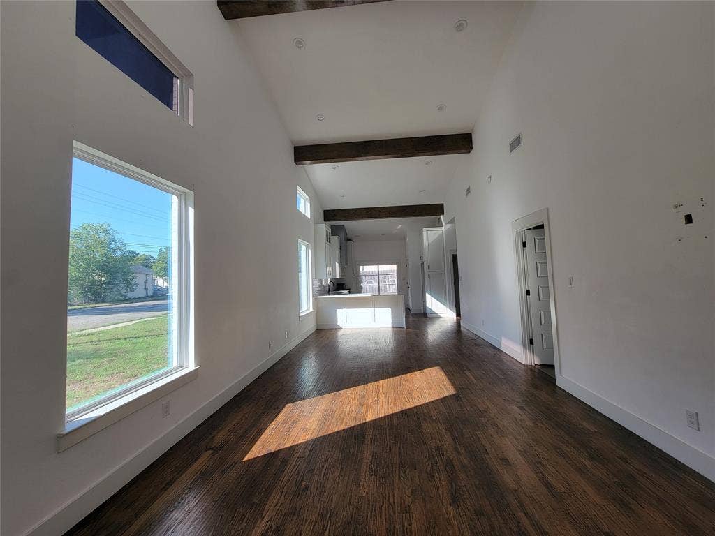 Vaulted ceiling with exposed wood beams, wood-finish flooring, and expansive windows
