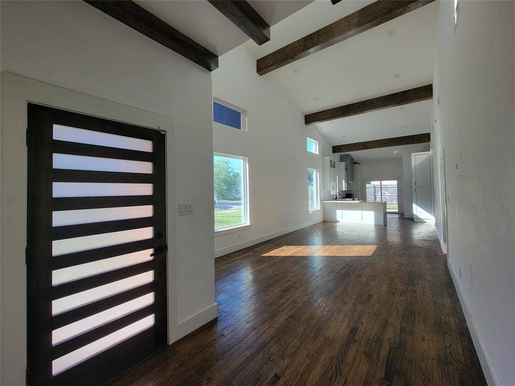 Vaulted ceilings featuring exposed wood beams, wood-finish flooring, and a modern entry door with horizontal frosted glass panes