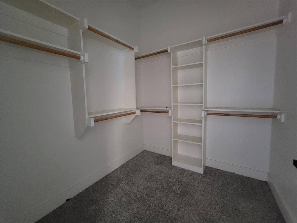 Custom walk-in closet featuring white built-in shelving, hanging rods, and neutral carpeting