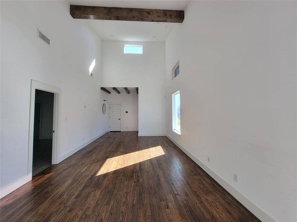 Vaulted ceiling featuring exposed wood beams, wood-finish flooring, and multiple natural light sources