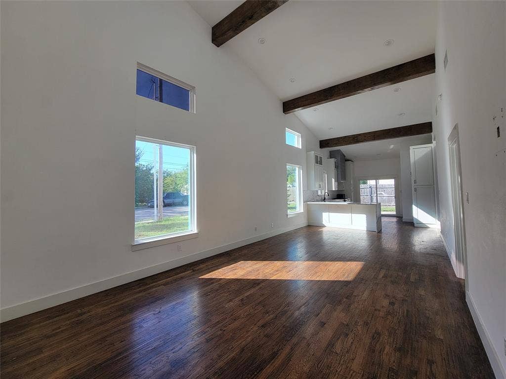 Vaulted ceilings with exposed structural beams, wood-finish flooring, and multiple oversized windows providing natural light