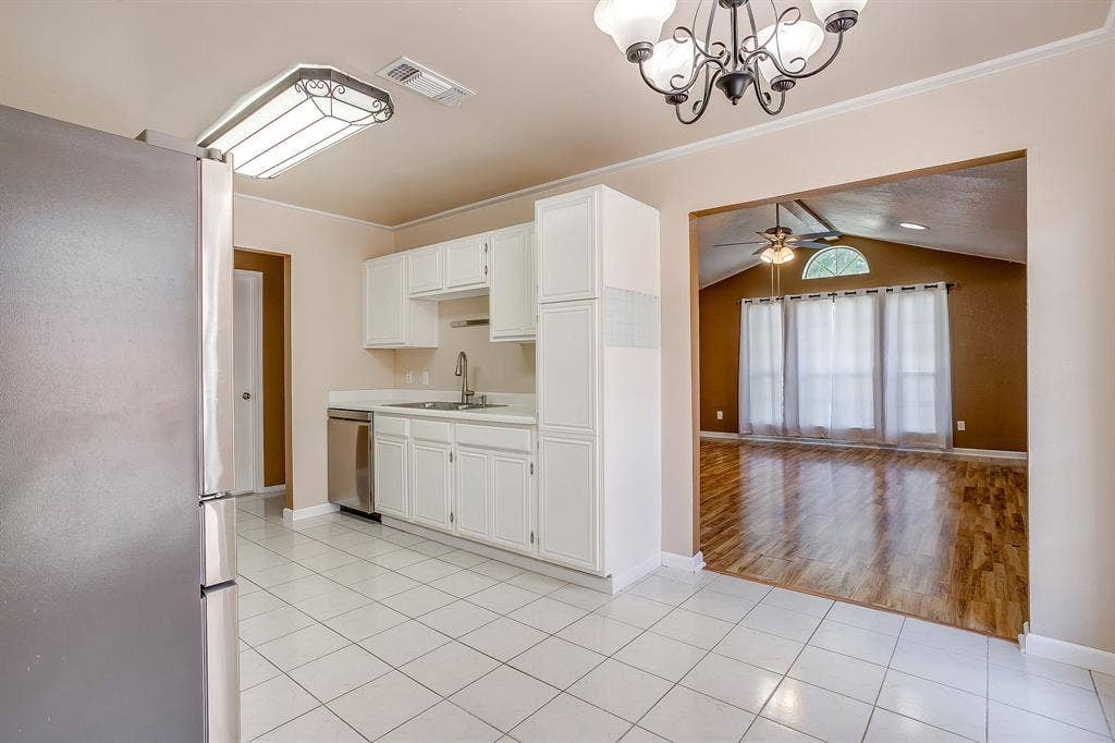 Kitchen featuring white cabinetry, stainless steel dishwasher, tile flooring, and integrated lighting, with wood-finish flooring in the secondary space