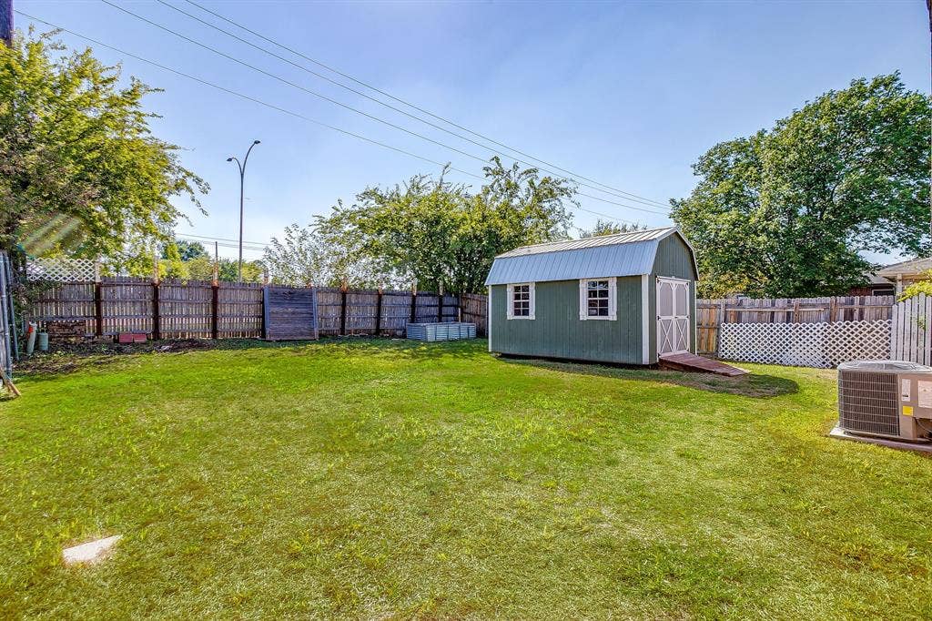 Backyard featuring a grass lawn, standalone storage building with a metal roof, and wood privacy fencing with lattice accents