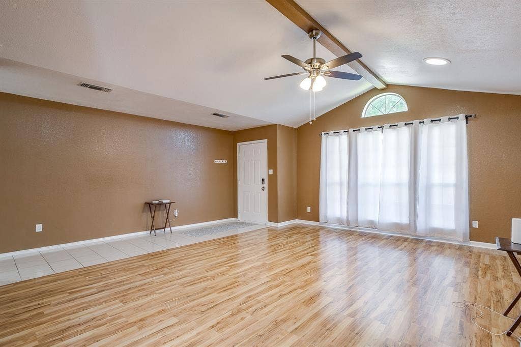 Vaulted ceilings featuring an exposed beam, wood-finish flooring, a multi-pane window with an arched transom, and a central ceiling fan