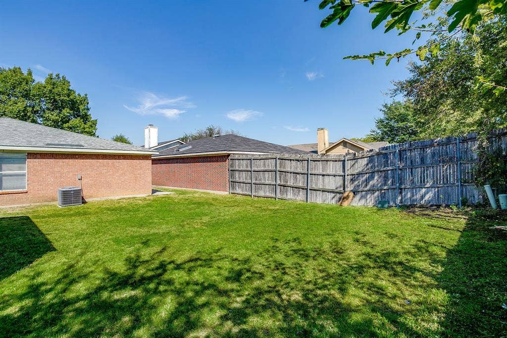 Backyard featuring a manicured lawn, brick exterior, and perimeter wood fencing
