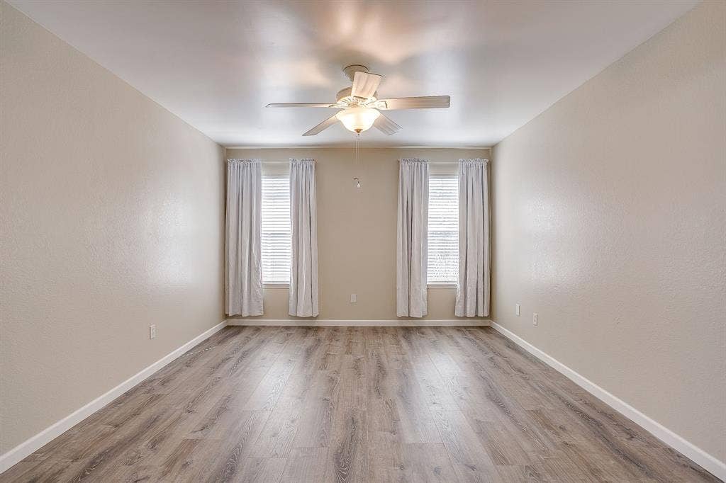 Room featuring wood-finish flooring, dual windows with blinds, and a centrally mounted ceiling fan with integrated light fixture