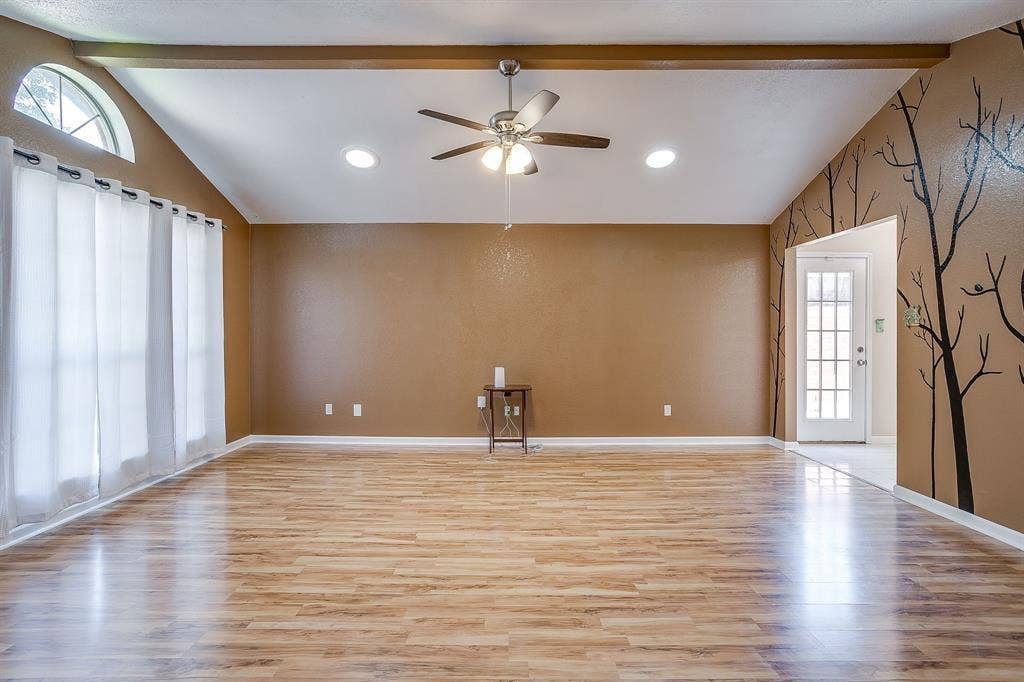 Vaulted ceiling featuring a central exposed structural beam, wood-finish flooring, recessed lighting, and a multi-pane arched window