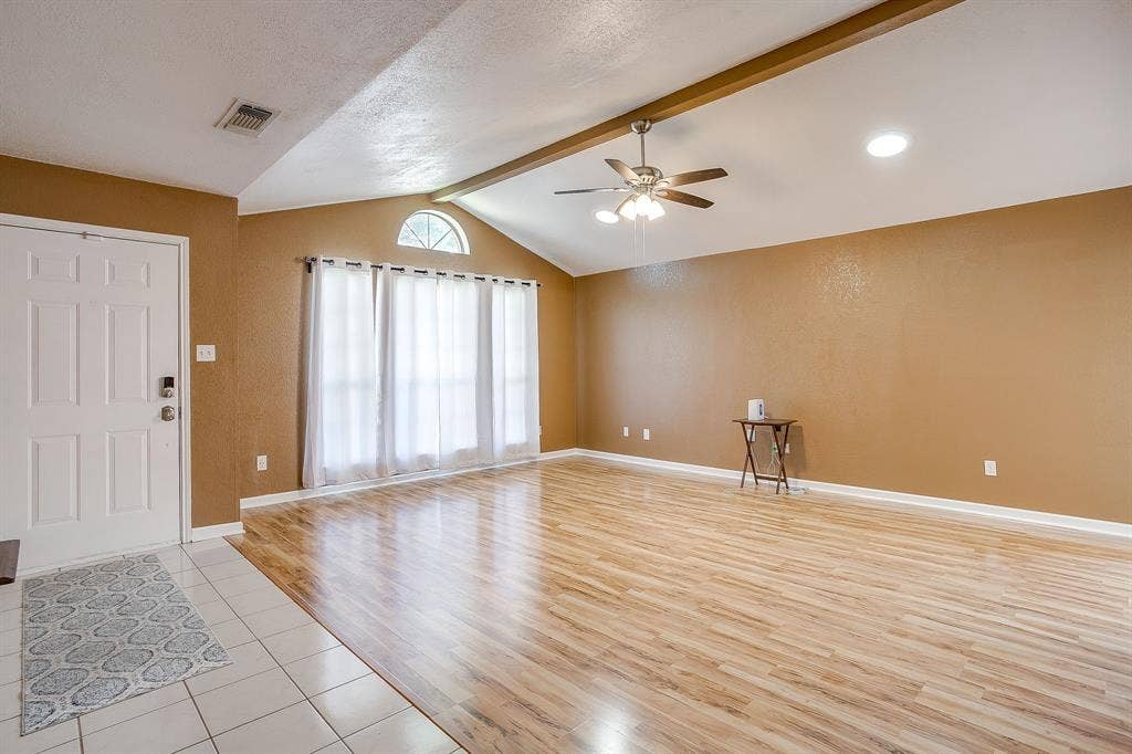 Vaulted ceiling featuring an exposed beam, wood-finish flooring, ceramic tile entryway, and multi-paned arched window