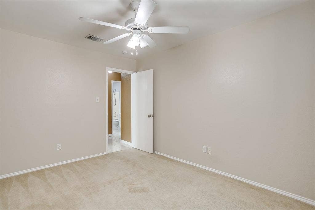 Neutral-toned interior space featuring light-colored wall-to-wall carpeting, a white ceiling fan with integrated lighting, and a six-panel door
