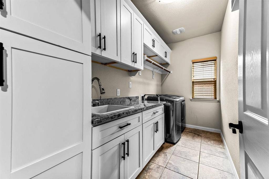 12467 Fallcreek Drive, Frisco, TX 75035 Laundry room featuring extensive white cabinetry, a utility sink, granite-style countertops, and tiled flooring