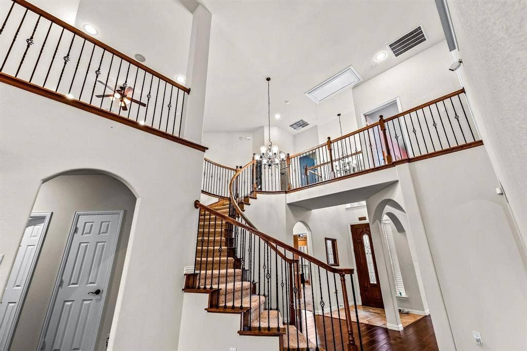 12467 Fallcreek Drive, Frisco, TX 75035 Two-story foyer with a grand curved staircase, wrought iron balusters, wood-finish flooring, and recessed lighting