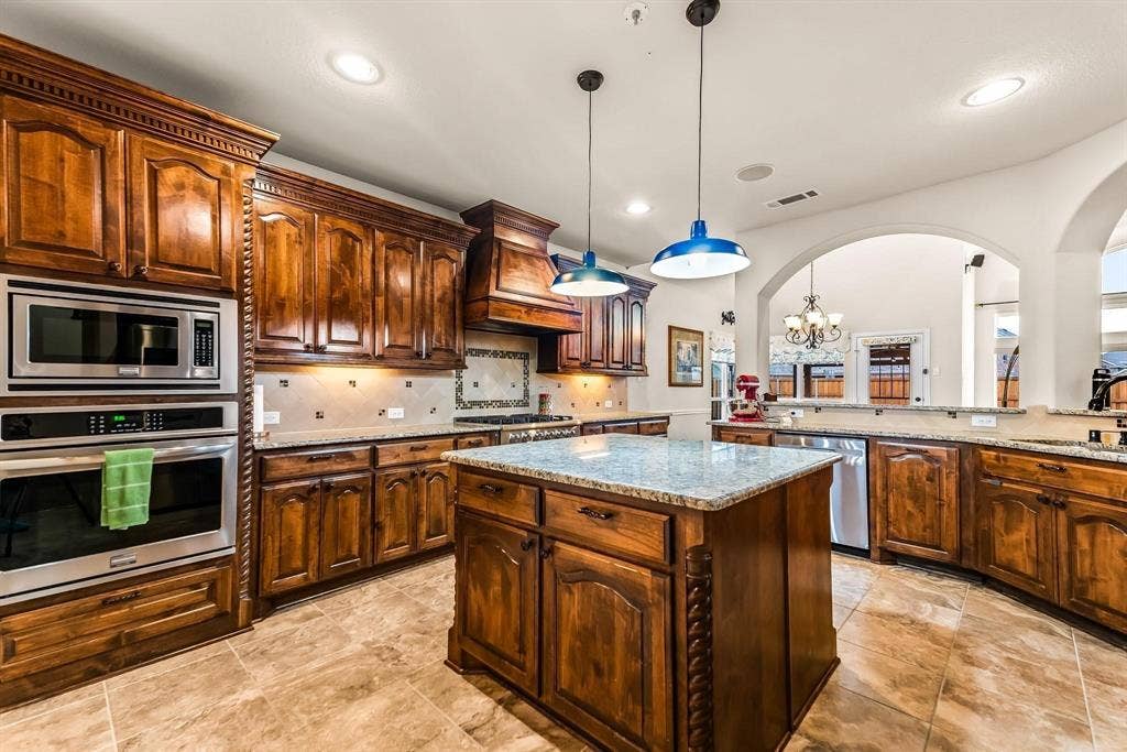 12467 Fallcreek Drive, Frisco, TX 75035 Custom wood cabinetry with ornate detailing, stainless steel built-in appliances, recessed lighting, a central island with a light-toned countertop, and tile flooring