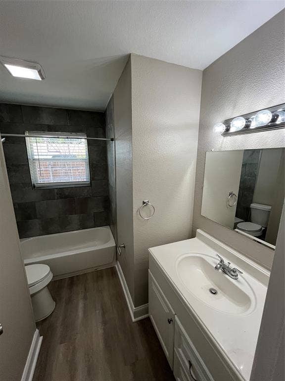 14206 Osage Drive, Balch Springs, TX 75180 Bathroom featuring wood-finish flooring, a white vanity with an integrated sink, a built-in bathtub with dark tile surround, and a chrome light fixture