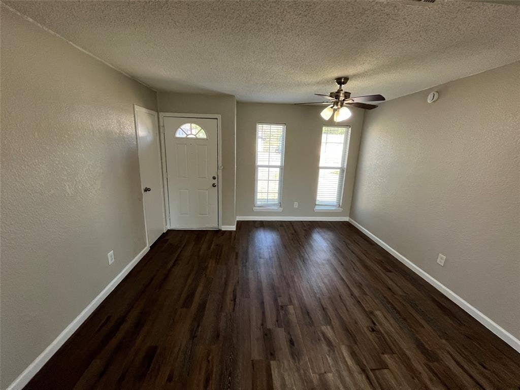 14206 Osage Drive, Balch Springs, TX 75180 Spacious room with dark wood-finish flooring, light neutral-toned walls, multiple windows, and a ceiling fan with integrated lighting