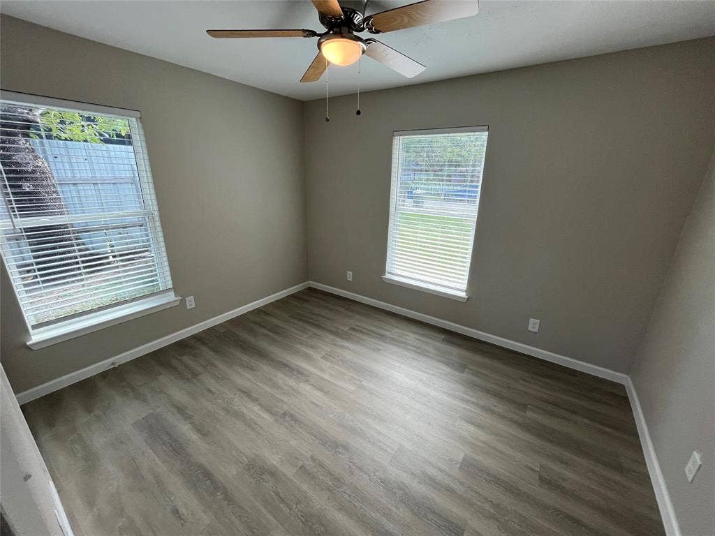 9527 Musgrave Drive, Dallas, TX 75217 Neutral-toned interior space featuring wood-finish flooring, dual windows with horizontal blinds, and a central ceiling fan with an integrated light fixture