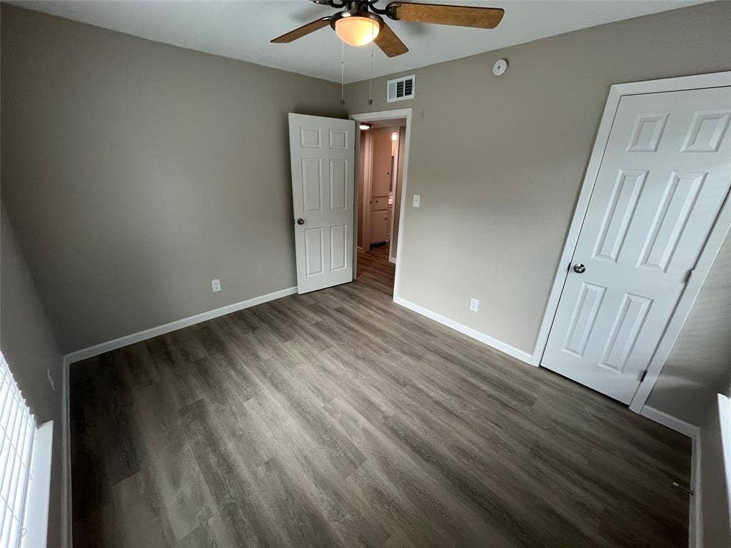 9527 Musgrave Drive, Dallas, TX 75217 Neutral-toned interior room featuring wood-finish flooring, a ceiling-mounted light fixture with a fan, and two interior doors