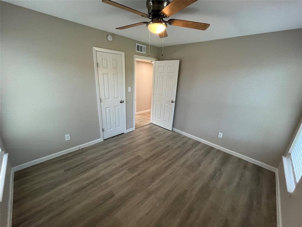 9527 Musgrave Drive, Dallas, TX 75217 Neutral-toned room featuring wood-finish flooring, a ceiling-mounted light fixture with fan, and two six-panel interior doors