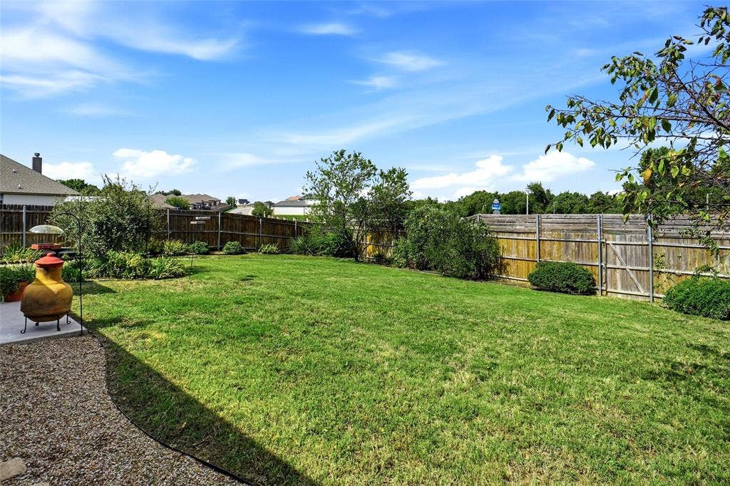 Expansive backyard featuring a level grass lawn, perimeter wood fencing, mature trees, and a gravel hardscape border