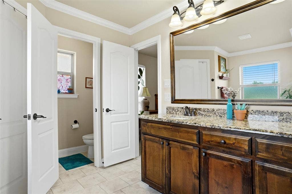 Bathroom featuring a wood vanity with stone countertop, large framed wall mirror, multi-bulb vanity lighting, and tile flooring