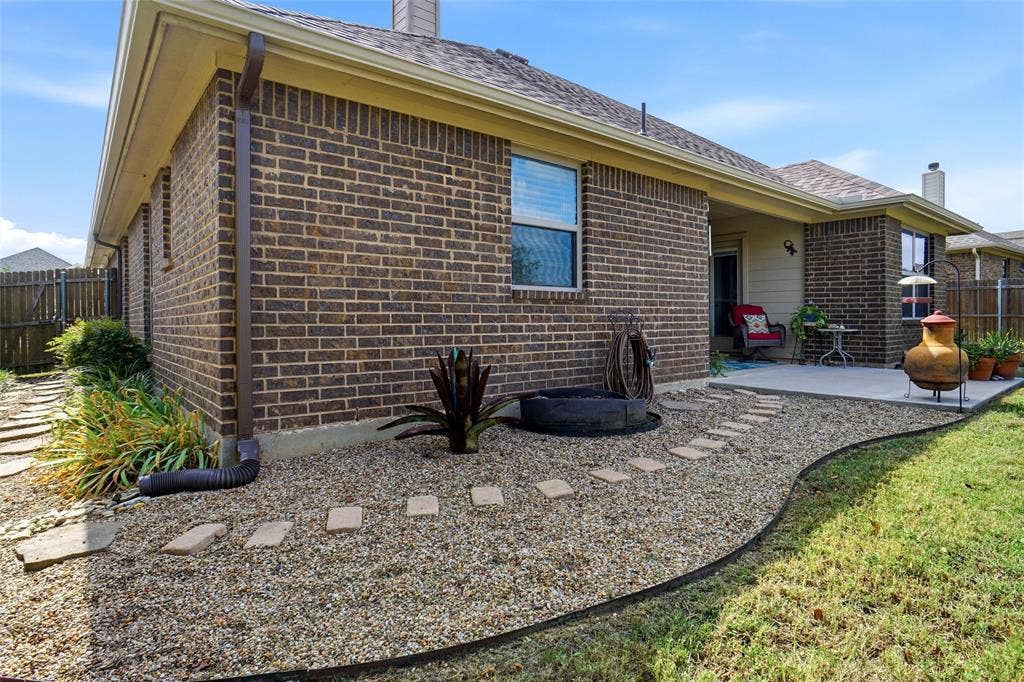 Brick exterior featuring a concrete patio, gravel landscaping with stone paver accents, and a wood privacy fence