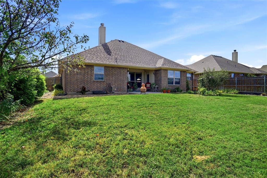 Backyard featuring a brick exterior, shingled roof, chimney, concrete patio, and fenced perimeter