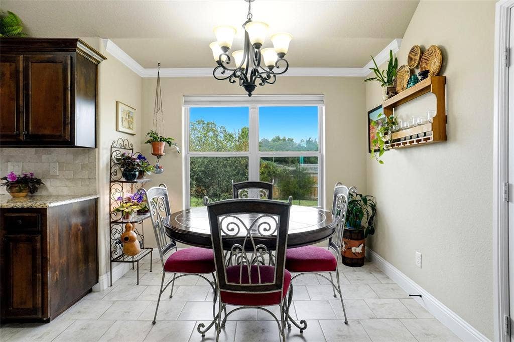 Dining area featuring neutral tile flooring, crown molding, a central multi-light chandelier, and natural light from a large window