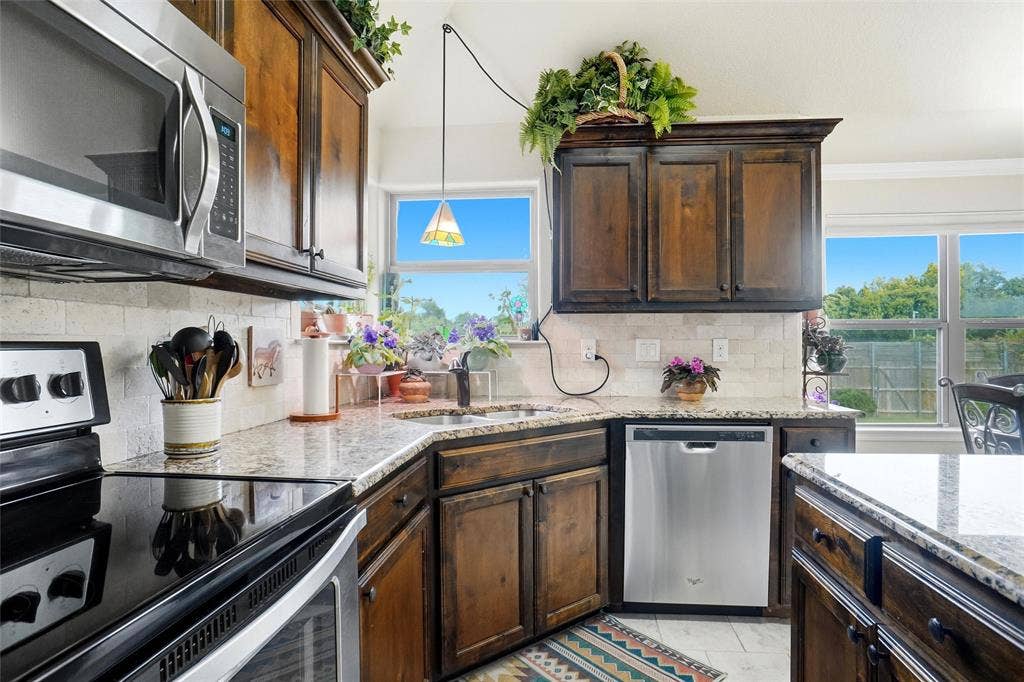 Kitchen featuring stained wood cabinetry, stone-finish countertops, stainless steel appliances, and a textured tile backsplash