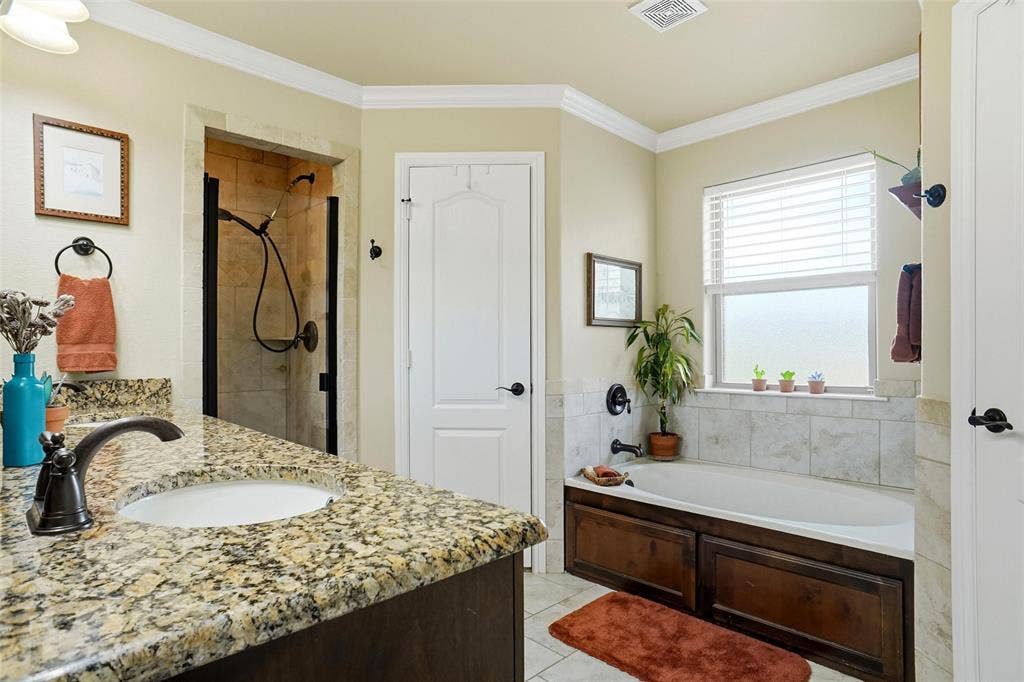 Bathroom featuring stone-surface countertop, under-mount sink with oil-rubbed bronze faucet, soaking tub with tile surround, and walk-in shower with tile walls