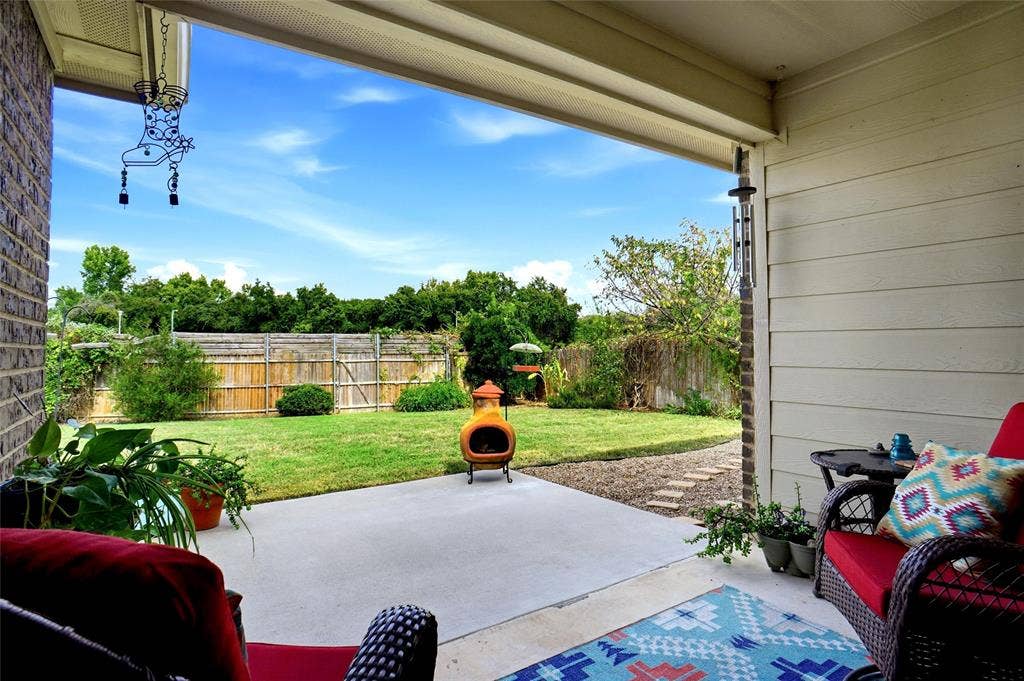 Covered concrete patio featuring brick exterior siding, horizontal lap siding, and a fenced backyard with mature landscaping
